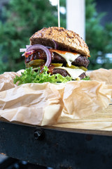 Burger na industrialnym stole w ekologicznym papierze. Duży lunch, burger meksykański grillowany na ogrodzie. Burger w bułce pełnoziarnistej. - obrazy, fototapety, plakaty