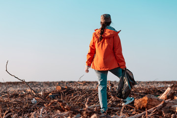 A young Caucasian female volunteer in a jacket stands with a garbage bag in her hands. In the...