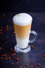 Latte macchiato in a tall glass. Glass of coffee latte and coffee beans on a dark background. Minimalism. Сopy space