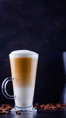 Latte macchiato in a tall glass. Glass of coffee latte and coffee beans on a dark background. Minimalism. Сopy space
