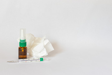 Close up of a nasal spray bottle, thermometer and tissue on a white background with blank space for text on the right, concept of flu and virus