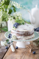 Homemade cherry cake with cream mascarpone on a light background and a bouquet of cherry flowers and lilacs. Vertical