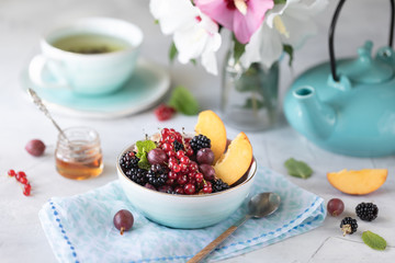 Granola or muesli with berries and fruits for a healthy breakfast in the morning with a bouquet of summer flowers on a light table. Horizontal