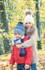 Two children - a small boy and a girl hugging against the background of autumn yellow leaves in Park. Concept of family, autumn, love, friendship.