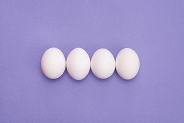 Close up overhead top view photo of four eggs in row with white shell isolated violet color background