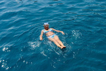 Aged woman is lying in sea water on her back.