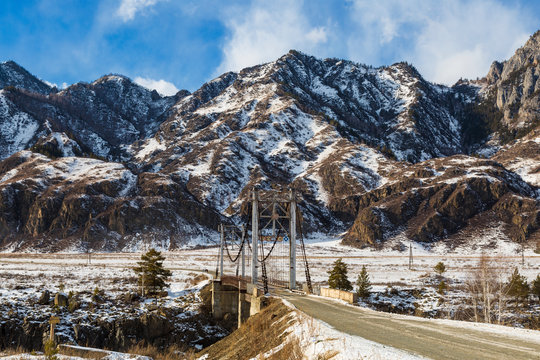 Suspension Road Bridge Over Katun In The Chemalsky District Of The Altai Republic In Winter. Russia