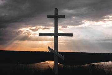 Cross In sunset light from dark clouds. Old wooden cross on hill in sunny rays over. Dramatic moody scenery. Belief and faith concept. Spiritual moment. Orthodox christianity.