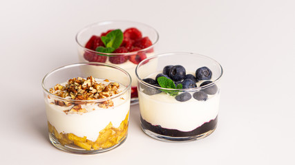 Three layer yogurt desserts: apple cinnamon and pecan nuts, blueberry jam, fresh blueberries, mint, raspberry jam and raspberries. White background. Concept: healthy living, sport nutrition, diet, 