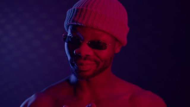 Black Guy In Dark Room With Sunglasses And Cap. Guy Raises His Glasses And Blinks.