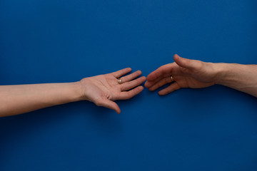 Female hand with a wedding ring reaches for a male hand with a wedding ring on a blue background. Concept support, help.