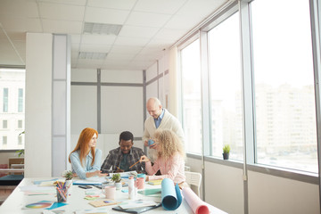Wide angle view at diverse business team discussing creative project during meeting at table in modern white office, copy space