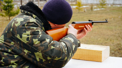 Man in camouflage uniform shooter shoots a rifle at a target