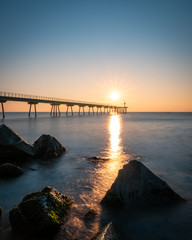 Fototapeta premium View of a sea dock at dawn from the beach with long exposure creating a silky smooth water