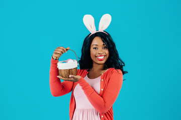 Portrait of a happy smiling mother with Easter eggs basket and bunny ears, isolated on blue...