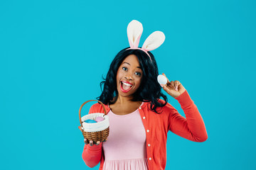 Portrait of an excited mother with Easter eggs basket and bunny ears, isolated on blue background