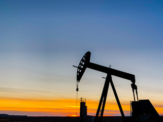 Black silhouette of an oilfield pumping unit at sunset.