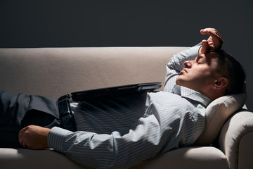businessman is lying on the sofa with laptop and resting