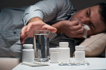 Overworked businessman is lying on the sofa and resting. Pills and glass of water near him.