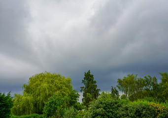 Obraz premium Dark grey stormy clouds over green trees