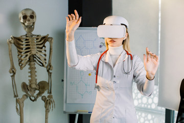 Young female doctor scientist using virtual reality glasses in clinic, working with virtual medical records of patients. Young girl medical student learning human anatomy using Vr Goggles