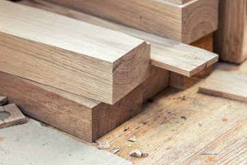 Oak wooden bar blocks materials stacked at carpentry woodwork workshop with tools and sawdust on...