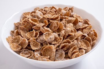Natural whole grain wheat flakes in white bowl. Healthy breakfast concept. Plate with multigrain flakes on white background