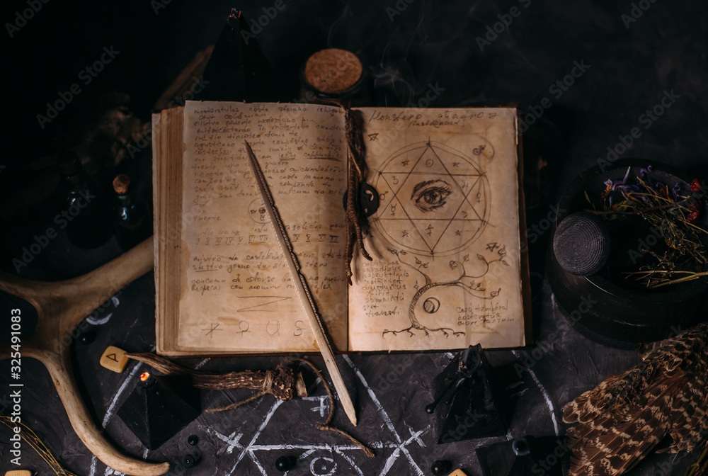 Wall mural Open old book with magic spells, runes, black candles on witch table. Occult, esoteric, divination and wicca concept.