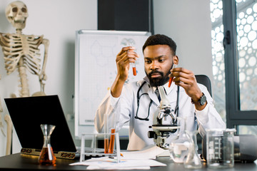 African man scientist, doctor, student works with test tubes in laboratory, conducting bio chemical...