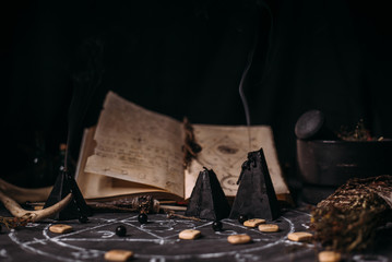 Open old book with magic spells, runes, black candles on witch table. Occult, esoteric, divination...