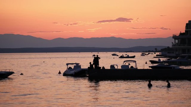 Sunset at Crikvenica, Croatia. Silhouettes of people in the water. Beautiful sunset sky. Crikvenica is a popular tourist resort, active fishing port and culture travel of Croatia. 4k. 60fps