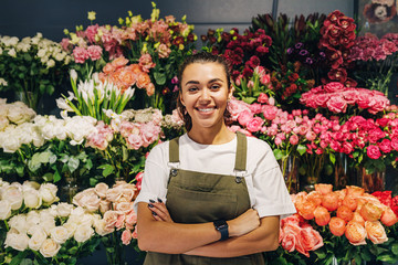 Woman florist standing in flower shop. Female florist in apron standing with her arms crossed. - obrazy, fototapety, plakaty