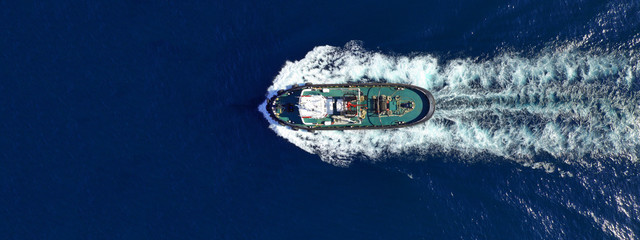 Aerial drone ultra wide top down photo of tug assisting boat cruising near Asian destination port