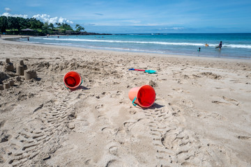 orange buckets with handles used to make sand castles on the beach with waves in distance