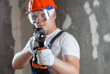 The builder with hammer drill perforator equipment making hole in wall at construction site. Repair...