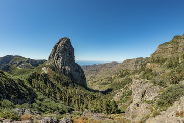 Fototapeta na wymiar Panoramic view of the Agando Rock in La Gomera island. A volcanic plug, also called a volcanic neck or lava neck, is a volcanic object created when magma hardens within a vent on an active volcano