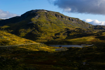 Landscape with mountains and a lake on a sunny day in Norway. Small house is on the lake’s coast....