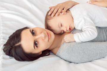 Fototapeta na wymiar Motherhood. Mother hugging sleeping baby lying on bed smiling happy close-up