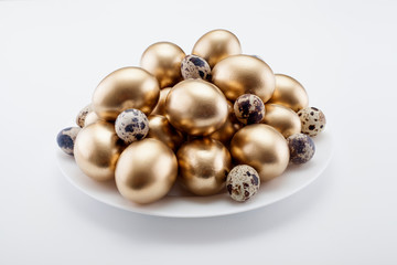 Golden eggs mixed with quail in a plate, on a white background. The concept of Easter, a symbol of the holiday, abundance and wealth.