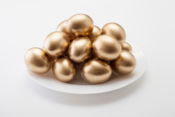 Golden eggs in a plate, on a white background. The concept of Easter, a symbol of the holiday, abundance and wealth.