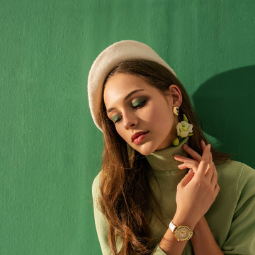 Close Up Portrait Of Young Beautiful Fashionable Woman With Green Eyeshadow Makeup, Wearing Turtleneck, White Beret, Wrist Watch, Posing On Mint Color Background. Copy, Empty Space For Text