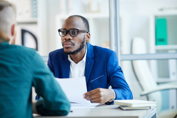Fototapeta premium Portrait of contemporary African-American businessman listening to candidate during job interview in office, copy space