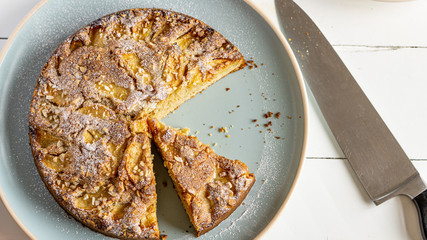 Sliced apple, almond and cinnamon pie on a round blue plate. There is knife near it on a table. Top view