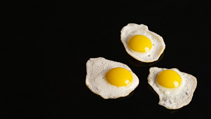 Three baked quail eggs on a black background. 