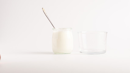 White natural yogurt in a glass jar with a spoon in it. Near there is a glass for yogurt. White background. 