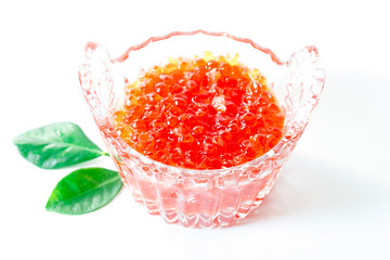 Red salmon caviar in a glass caviar bowl is decorated with green leaves on a white background