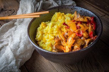 Saffron rice with pieces of chicken and vegetables on wooden table.