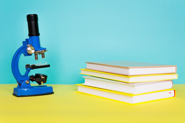 Blue microscope with books on a yellow table. The concept of schooling, research, discovery.