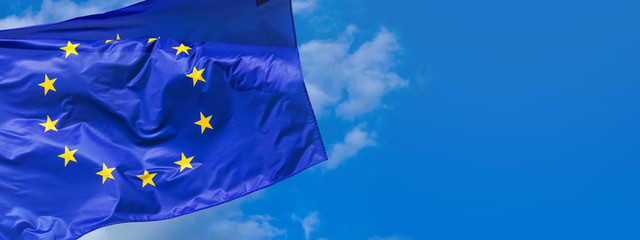 Flag of the European Union waving in the wind on flagpole against the sky with clouds on sunny day, banner, close-up