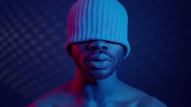 Black Guy In Room With Blue Lighting. On His Head Cap That Closes His Eyes.